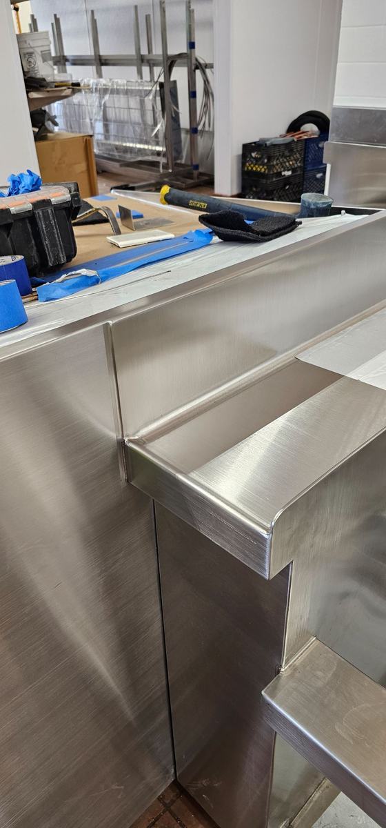 Edge of a custom stainless steel counter with a raised rim and shelf