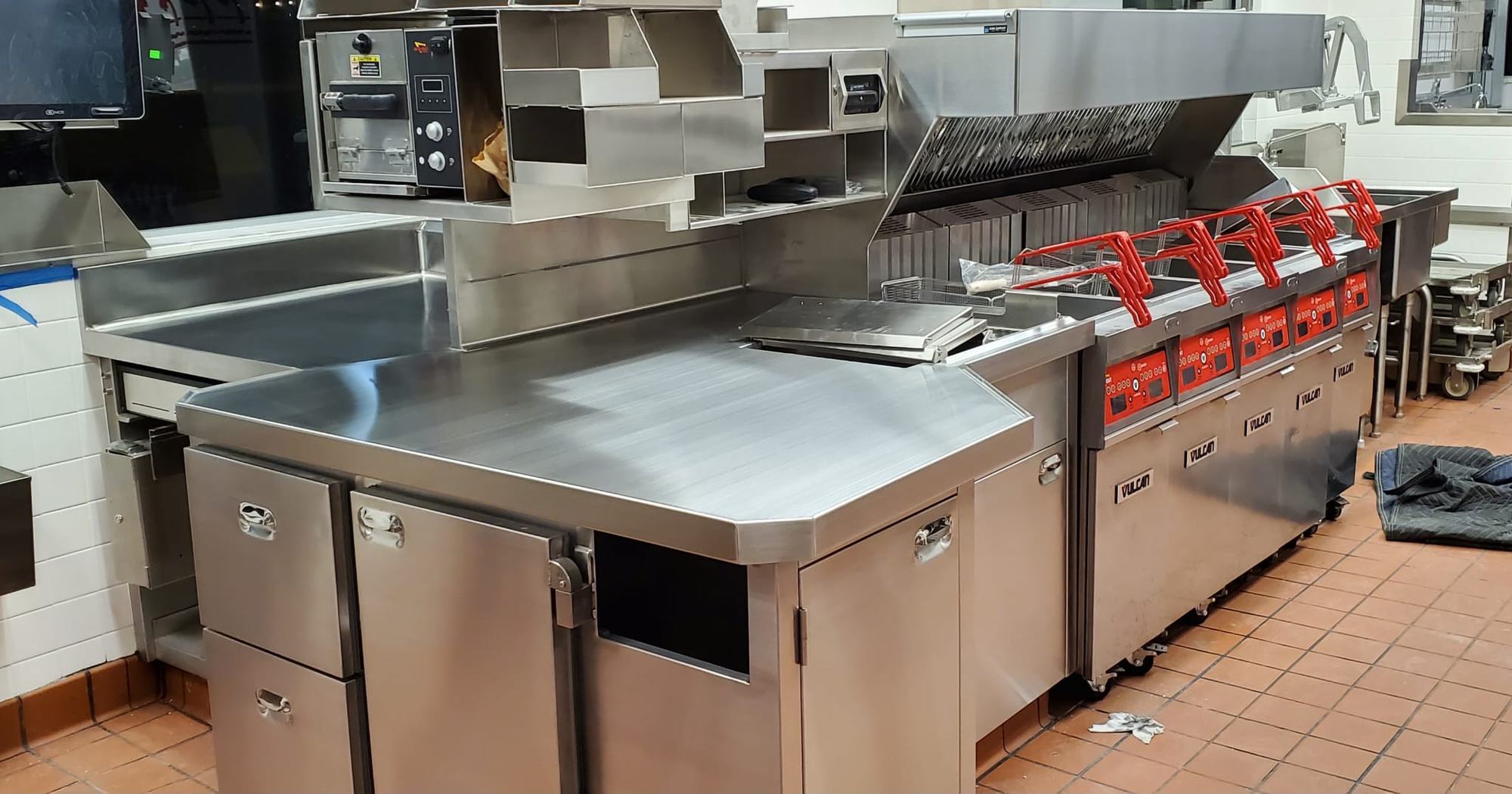 A commercial kitchen line installed by Benitez Stainless Steel: stainless prep tables, fryers and a wall hood