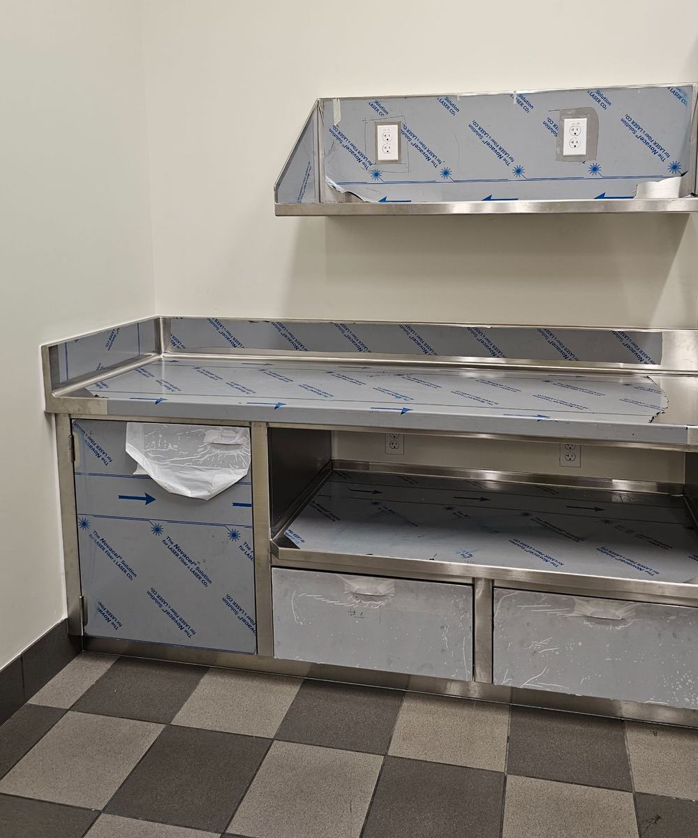 Stainless steel prep table and wall hood, still in protective film, on a checkered tile floor