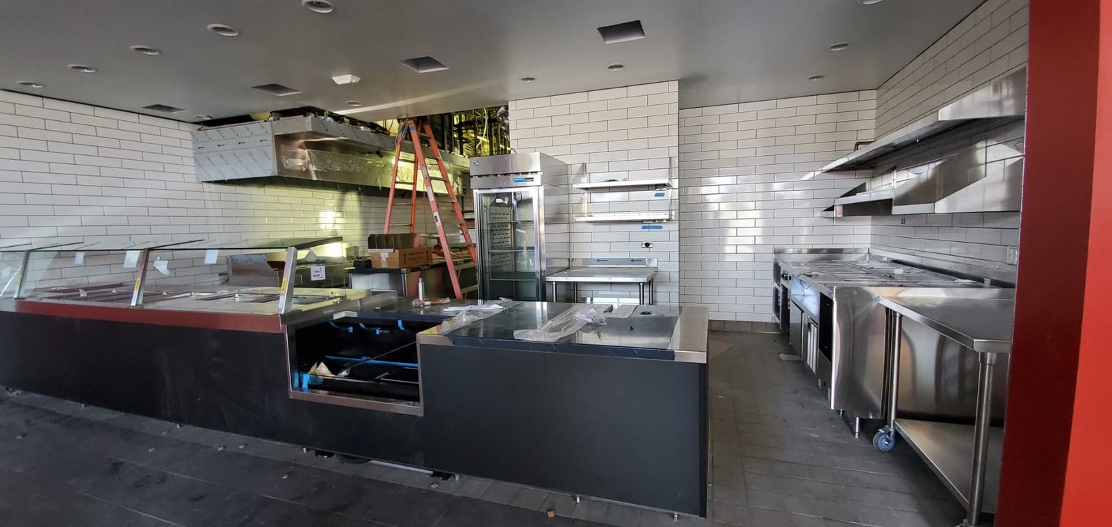 Commercial kitchen with white subway tile, stainless counters and a serving line under construction