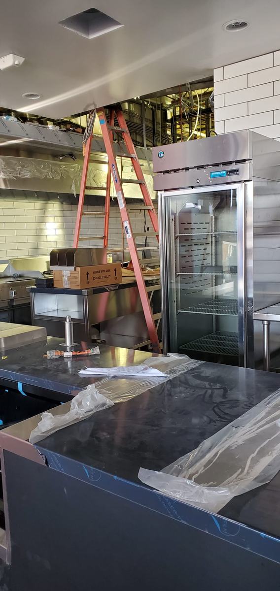 School kitchen during installation with a stainless prep line, an upright oven and a ladder